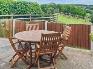 A round wooden table with four chairs, a wooden fence, and a view of a green landscape.