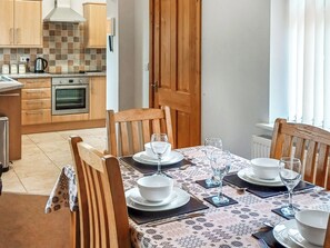 A dining area with a table set for four, wooden chairs, and a view of the kitchen in the background. - 2 bedroom accommodation in Prion, near Denbigh (Prion, near Denbigh)
