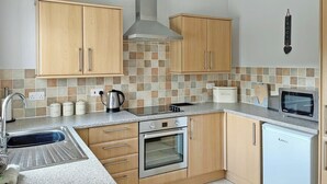 A kitchen with wooden cabinets, a stainless steel oven, a microwave, and a small refrigerator. - 2 bedroom accommodation in Prion, near Denbigh (Prion, near Denbigh)