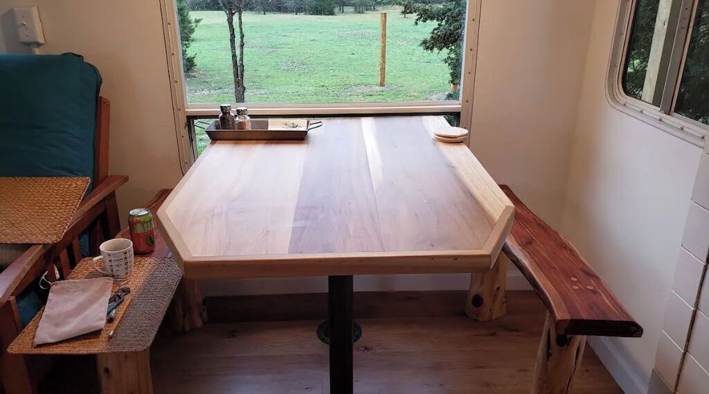 Una cocina pequeña y rústica con una mesa de madera, un banco y una ventana con vistas a una zona de césped.