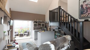 Een ruime woonkamer met een trap, een eethoek en uitzicht door een glazen deur.