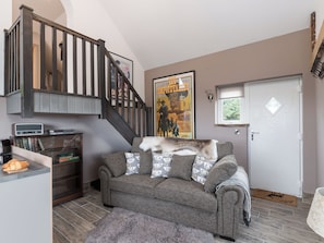 A living room with a staircase, a poster on the wall, a white door, and a small rug.