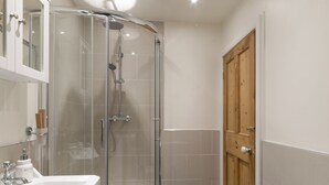 Een badkamer met een douche met glazen wand, een witte badkuip en een houten deur.