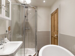 Een badkamer met een douche met glazen wand, een witte badkuip en een houten deur.