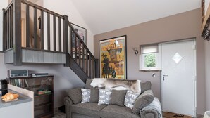Een woonkamer met een trap, een poster aan de muur, een witte deur en een klein vloerkleed.