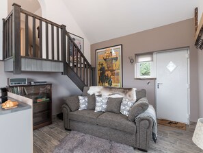 Een woonkamer met een trap, een poster aan de muur, een witte deur en een klein vloerkleed.