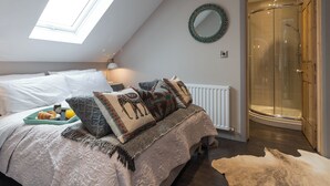 Een slaapkamer met dakraam, een bed met beddengoed met een patroon, een nachtkastje met lamp, een spiegel en een douchehoek.