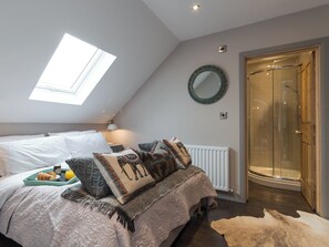 Een slaapkamer met dakraam, een bed met beddengoed met een patroon, een nachtkastje met lamp, een spiegel en een douchehoek.