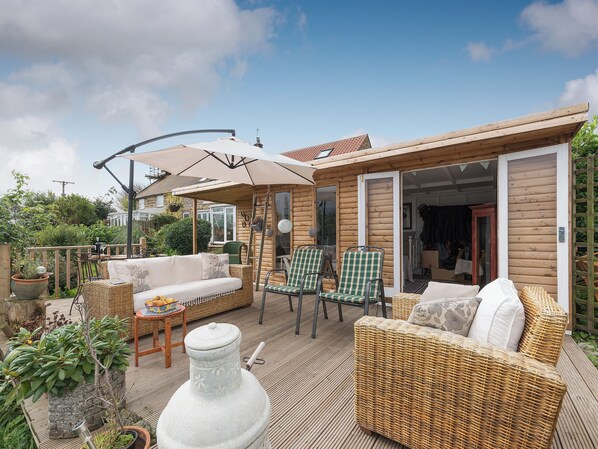 A wooden cabin with a patio area, wicker furniture, and a large umbrella.