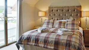 A bedroom with a tufted headboard, a plaid bedspread, two bedside lamps, and a view through a glass door. - 5 bedroom accommodation in Aviemore (Aviemore)