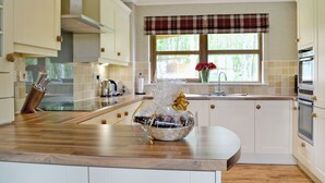 A modern kitchen with wooden countertops, white cabinetry, a built-in oven, and a window with a plaid valance. - 5 bedroom accommodation in Aviemore (Aviemore)