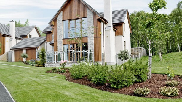A two-story house with a stone facade, wooden trim, and a fenced front yard with various plants. - 5 bedroom accommodation in Aviemore (Aviemore)