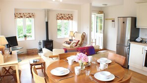 A modern kitchen with a built-in stove, a dining area with a round wooden table set for four, and a cozy living area with a fireplace. - Quiet rural idyll near Salisbury. (Near Salisbury)