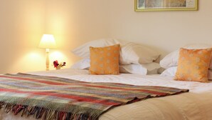 A neatly made bed with white linens and two orange pillows, a colorful striped blanket, a bedside lamp, and a framed artwork on the wall. - Quiet rural idyll near Salisbury. (Near Salisbury)