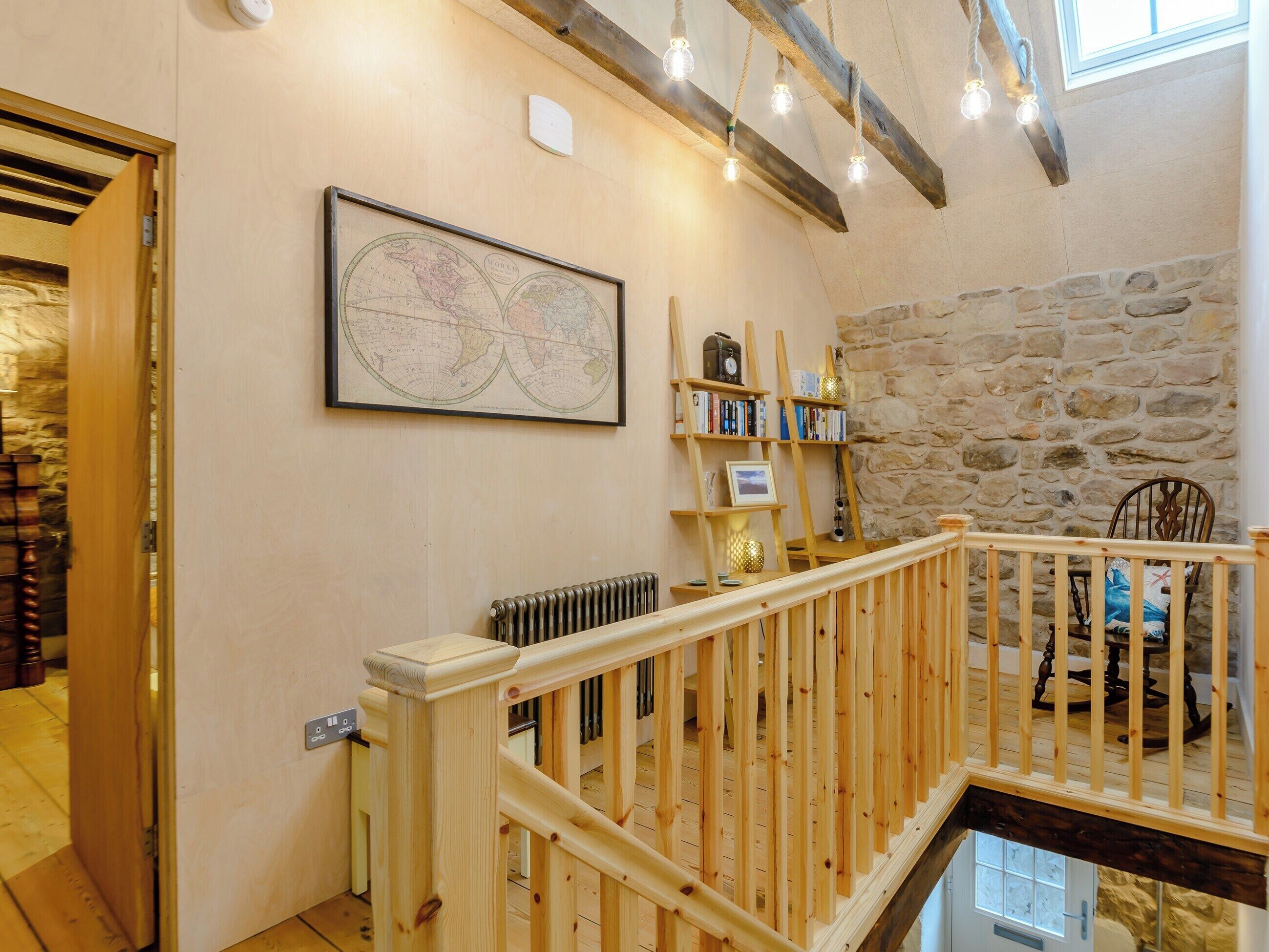 A wooden staircase with a railing leading to a loft area. A world map is displayed on the wall, and a bookshelf is visible.