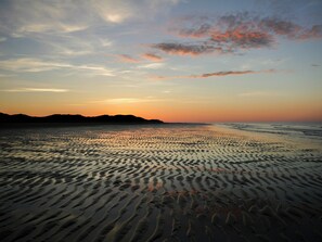 Ein Strand mit gewellten Sandmustern und einem Sonnenuntergang im Hintergrund.