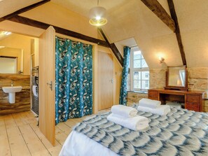 Ein Schlafzimmer mit einem großen Bett, einer Holzkommode, einem Spiegel und einem Badezimmer mit Waschbecken und Dusche.