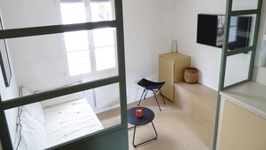 Een kamer met een bed, een klein tafeltje met een kaars, een stoel, een kast en een aan de muur bevestigde televisie.