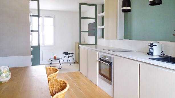 Een moderne keuken met witte kastjes, een houten eettafel, rieten stoelen en een groot raam.