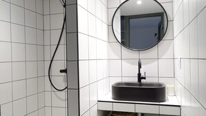 Een badkamer met witte betegelde wanden, een ronde spiegel, een zwarte wastafel en een douchekop.