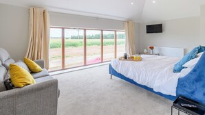 Ein Schlafzimmer mit Bett, Sofa, Fernseher und Blick auf ein Feld.