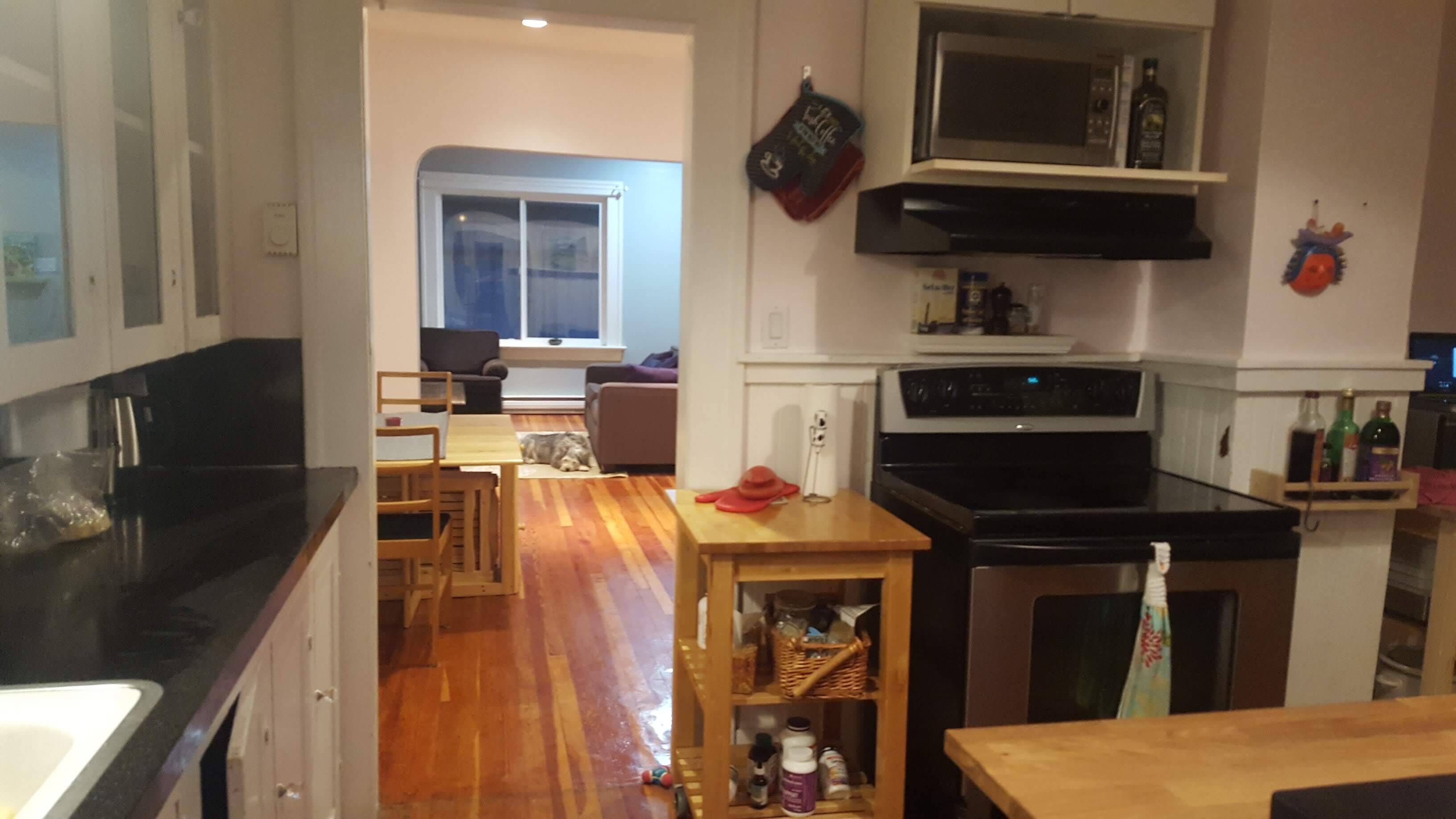 Una cocina con suelo de madera, un comedor con mesa y sillas, un microondas y una estufa.