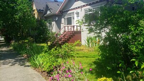 A residential house with a visible staircase leading to the entrance, surrounded by lush greenery and flowering plants. - Sunlit Craftsman Home | Steps to Cafes and restaurants | 10 mn to downtown (Vancouver)