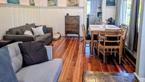 A living room with a sofa, a dining table with chairs, wooden flooring, and artwork on the walls. - Sunlit Craftsman Home | Steps to Cafes and restaurants | 10 mn to downtown (Vancouver)