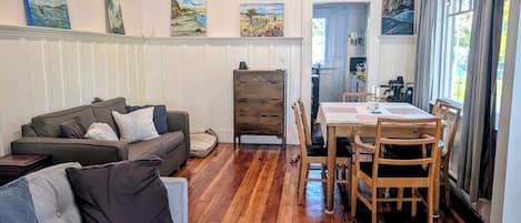 Una sala de estar con un sofá, una mesa de comedor con sillas, suelo de madera y obras de arte en las paredes.