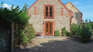 A stone house with a wooden door and two windows, surrounded by greenery. - 1 bedroom accommodation in Holt (Holt)