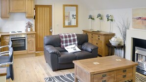 A living room with a sofa, wooden coffee table, and a fireplace. There is a kitchen area with wooden cabinets and an oven. - 1 bedroom accommodation in Holt (Holt)