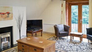 A living room with a fireplace, a television, a leather armchair, and a patterned rug. - 1 bedroom accommodation in Holt (Holt)