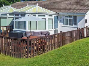 A house with a covered patio, a wooden deck, and a lawn.