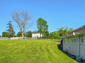A well-maintained grassy yard with a white building, a large tree, and a fence.