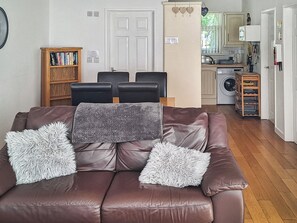 A brown leather sofa with fluffy pillows, a wooden bookshelf, and a kitchen area with a washing machine.
