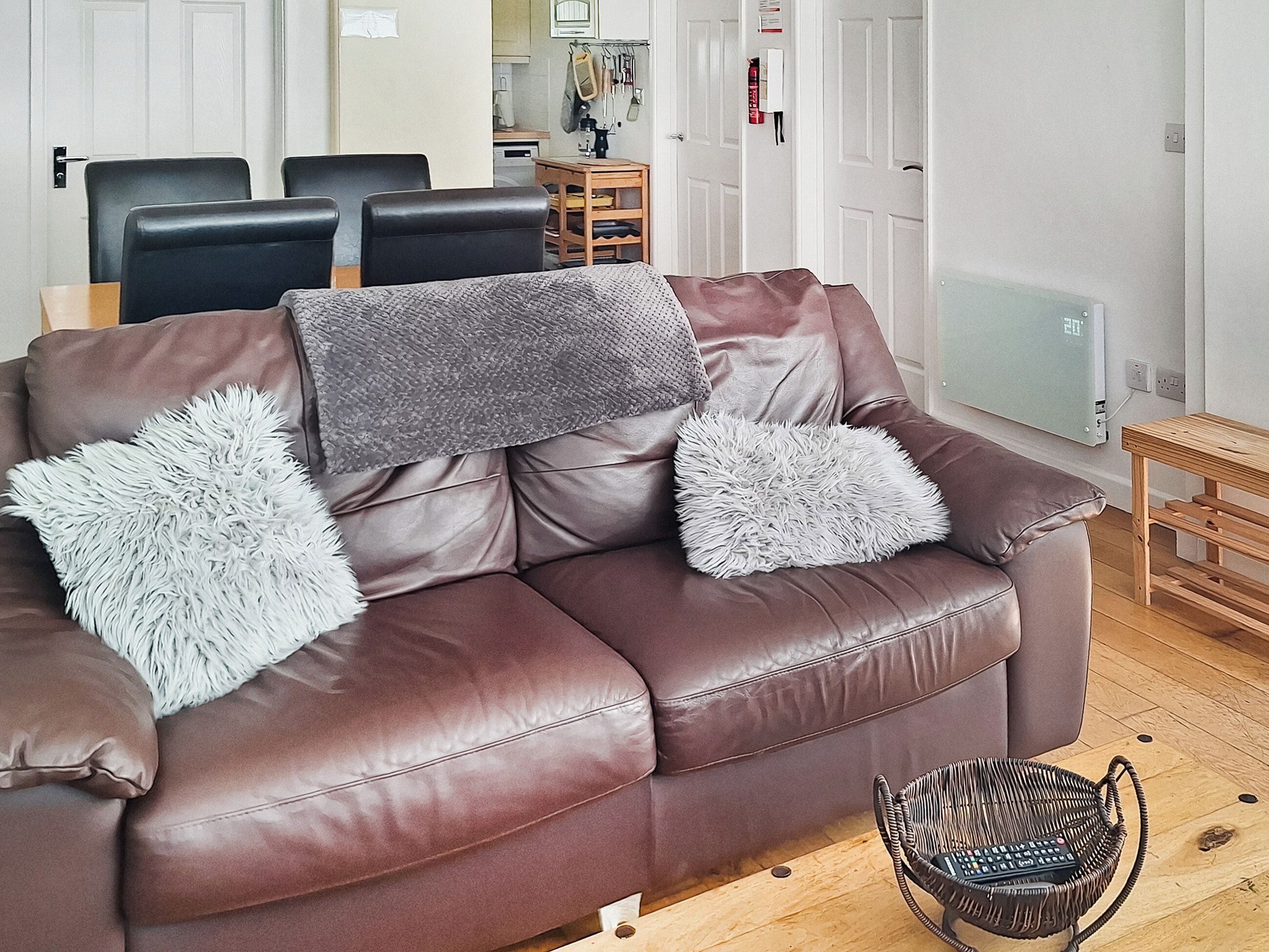 A brown leather sofa with two fluffy white pillows and a grey throw blanket.