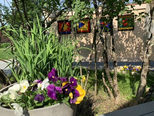 A garden with a variety of flowers and trees, a concrete planter, and a building with colorful wall decorations.