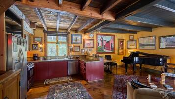 A spacious living area with a piano, a dining table, and a kitchen with red cabinets and wooden beams.