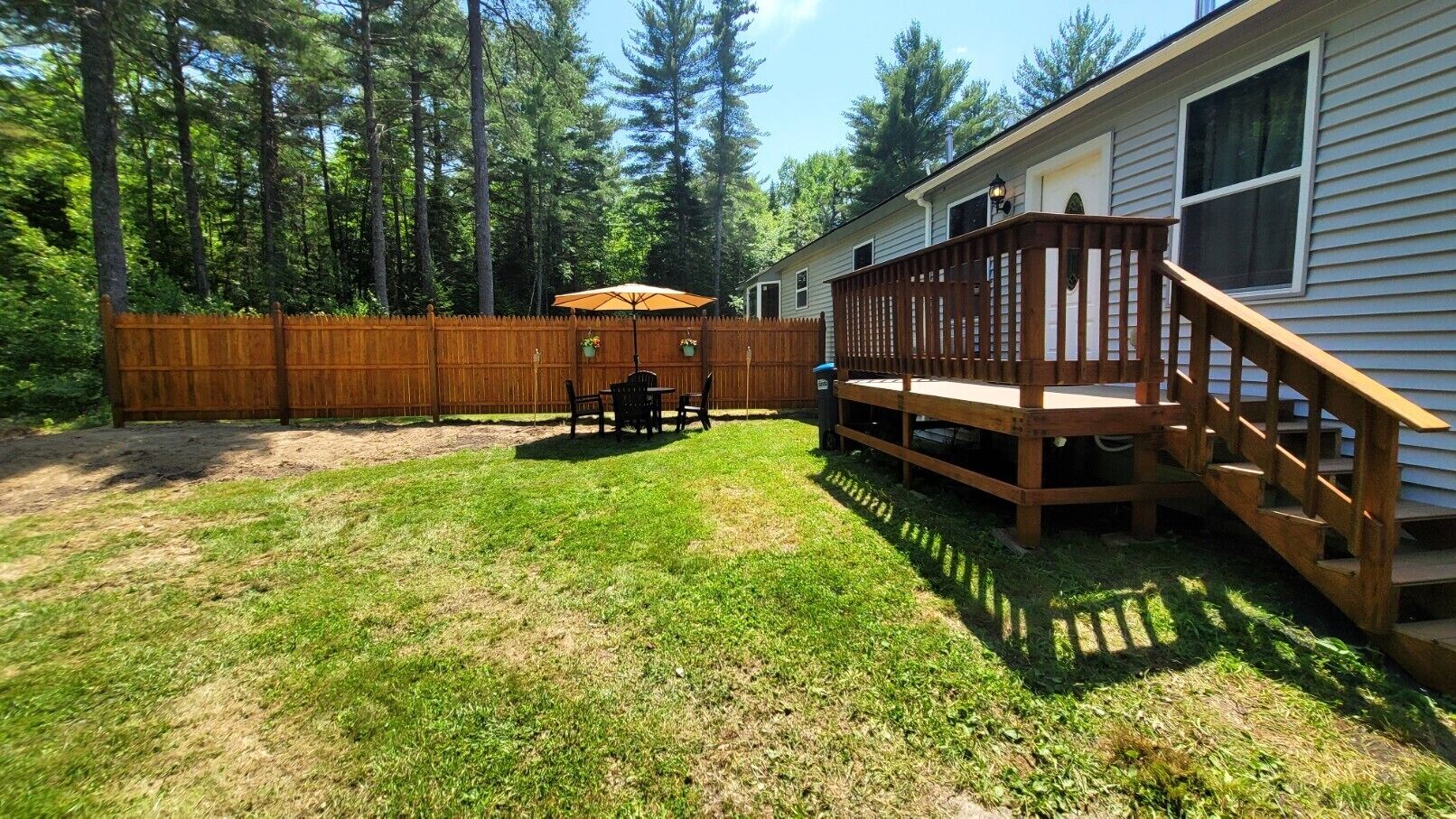 A backyard with a wooden deck, a patio table, and a wooden fence.