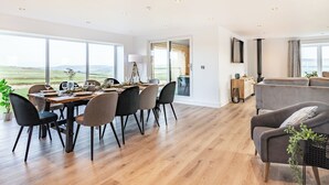 A modern dining area with a view of the countryside, a cozy living room with a sofa, and a large window. - Hazelgrove Lodge Barn (Laneshawbridge)