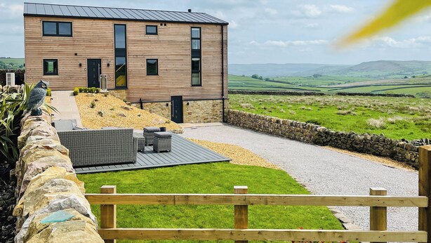 A modern two-story house with a stone foundation, a paved patio, and a view of rolling hills. - Hazelgrove Lodge Barn (Laneshawbridge)