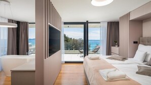 Ett modernt hotellrum med en stor säng, ett badkar och en balkong med utsikt över havet.