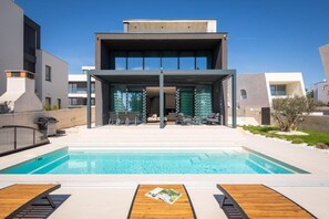 Una casa moderna con piscina, zona de estar exterior y patio cubierto.
