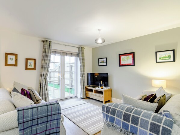 A living room with two sofas, a TV, a wooden side table, and a large window with curtains.