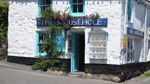 En vit byggnad med en skylt som visar texten ”THE MOUSEHOLE” och en utställning av muggar i fönstret.