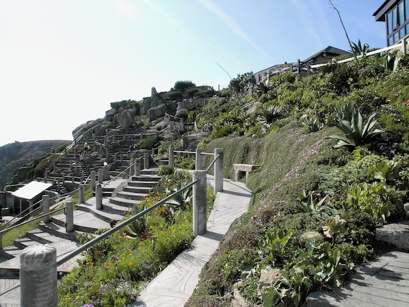 A set of stone stairs leading up a hillside with a garden and a building in the background.