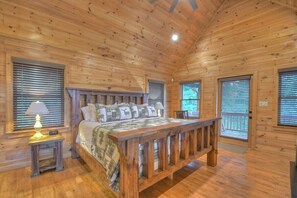 A wooden cabin bedroom with a bed, a nightstand, a lamp, and a window with blinds. - Casa Con Vista | Mtn Views + Hot Tub + Game Room (Epworth)