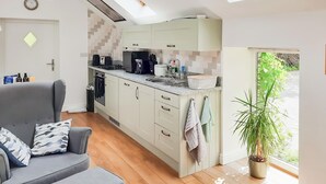 A compact kitchen with a dining area, featuring a grey sofa, a potted plant, and a view through a glass door.