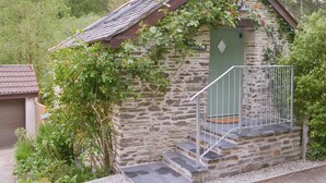 A stone building with a sloped roof, a green door, and a small staircase leading to a balcony.