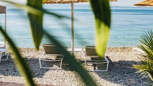 Eine Strandlounge mit zwei Liegestühlen und einem Reetdach-Sonnenschirm mit Blick auf das ruhige Meer.